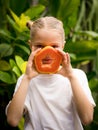 Charming little girl with fresh papaya. Caucasian girl holding slice of papaya fruit in front of her face. Selected focus. Green Royalty Free Stock Photo