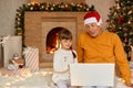 Charming little girl with grandfather sitting on floor and using laptop computer for video call during Christmas, family posing in Royalty Free Stock Photo