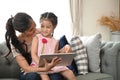 Charming little girl and her beautiful young mom are using a digital tablet on couch. Royalty Free Stock Photo