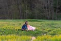 Charming little girl with long hair in denim jacket collects garbage in nature, in park, in meadow on summer day.