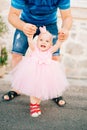 A charming little girl in a pink dress, sneakers and with a crown on her head holding dad by the hands and laughing Royalty Free Stock Photo