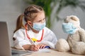 Charming little girl in a white coat and mask, treats a Teddy bear