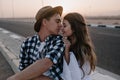 Charming long-haired girl posing with her stylish boyfriend in trendy hat, gently touching his shoulder. Portrait of Royalty Free Stock Photo