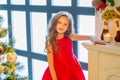 Charming Long Haired Girl in Red Dress Standing in front of Window. Royalty Free Stock Photo