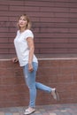 Charming mature woman, 50-55 years old, blonde, dressed in torn jeans, stands against the background of a brick wall