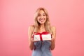 Charming millennial lady holding gift box with ribbon, receiving Woman& x27;s Day or birthday surprise on pink background