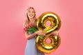 Charming millennial lady with spring flowers and gold balloon celebrating Woman& x27;s Day on pink studio background