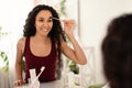 Charming millennial woman applying eyebrow mascara near mirror at home, empty space Royalty Free Stock Photo