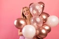 Charming millennial woman with bunch of air balloons having holiday party over pink studio background