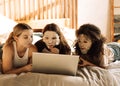 Charming mixed-race teenagers in cosmetic fabric masks on their faces are looking at laptop. Multiethnic friends have fun and use Royalty Free Stock Photo