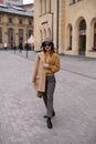 Charming model girl in an autumn beige coat and sunglasses, plaid panama hat standing with face turned holding coat on