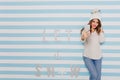 Charming model of 23 years with charming smile makes photo on iPhone. Full-length portrait on striped background.