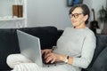 Charming modern senior woman using laptop sitting on comfortable couch Royalty Free Stock Photo