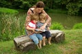 Charming Mother Reading a Book to Her Adorable Little Twin Sons While Sitting Outside Near Beautiful Lake