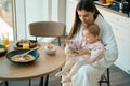 Charming mother sits with her little daughter at kitchen table