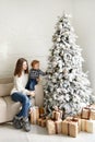 Charming mother in the white sweaterholding her little toddler son near Christmas tree and gift boxes in living room in the house Royalty Free Stock Photo