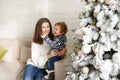 Charming mother in the white sweaterholding her little toddler son near Christmas tree in the house Royalty Free Stock Photo