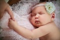 Charming newborn baby with a flower on her head sleeps on a pink knitted plaid holds moms finger
