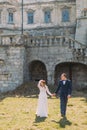 Charming newlywed bride and groom holding hands on green lawn near beautiful ruined baroque palace Royalty Free Stock Photo