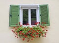 Charming old window with green shutters and red geraniums flowers Royalty Free Stock Photo