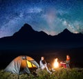 Charming pair tourists sitting by bonfire under incredibly beautiful starry sky, Milky way. Astrophotography