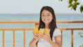 A charming philippine schoolgirl girl in a white dress and long hair positively poses with a mango in her hands. The sun