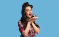 Charming pinup lady in retro wear eating chocolate cake on blue studio background Royalty Free Stock Photo