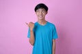 Charming pleased young Asian man smiling points aside on copy space shows advertisement wears casual clothes against pink Royalty Free Stock Photo