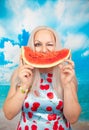 Charming plump blonde in pin up dress stands with a piece of watermelon and enjoys rest and a snack