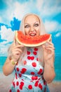 Charming plump blonde in pin up dress stands with a piece of watermelon and enjoys rest and a snack