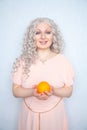 Charming plump curly blonde in pink dress with orange on white solid studio background alone