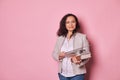 Charming positive middle aged female educator holding eyeglasses, studying books and pointer, smiles looking at camera