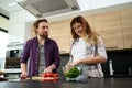 Charming pregnant young woman preparing vegetable salad with her husband in home kitchen. Caucasian heterosexual couple enjoy Royalty Free Stock Photo