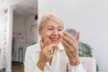 Charming, pretty, old woman touching her perfect soft face skin with fingers, smiling at camera over gray background, using day, Royalty Free Stock Photo