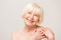Charming, pretty, old woman touching her perfect soft skin with fingers, smiling at camera over gray background, using day, night Royalty Free Stock Photo