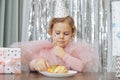 Charming, red-haired baby in party hat and pink chiffon outfit 4-5 years old is trying delicious cake for her Royalty Free Stock Photo