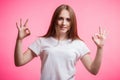 A charming red haired girl with two hands showing OK sign on pink background. Good mood, luck, happiness and emotion concept.