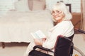 Charming retired lady reading book in wheelchair at home