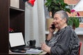 charming senior business woman talking on phone and smiling while working with a laptop at home Royalty Free Stock Photo