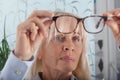 Charming senior woman lifting up her eyeglasses and checking their cleanliness