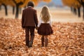 A boy and girl walk hand in hand through a pile of autumn leaves