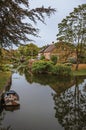 Charming small canal next to rustic house with lush garden and trees reflected on the water in cloudy day at Drimmelen.