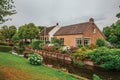 Charming small canal next to rustic houses with lush flowery garden and lawn in cloudy day at Drimmelen. Royalty Free Stock Photo