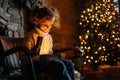 Charming smiling little blonde child girl opening magical Christmas box with gift sitting on rocking chair in xmas Royalty Free Stock Photo