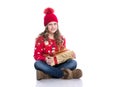 Charming smiling little girl with curly hairstyle wearing red knitted sweater and hat holding christmas gift isolated on white. Royalty Free Stock Photo