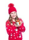 Charming smiling little girl with curly hairstyle wearing red knitted sweater and hat holding christmas gift isolated. Royalty Free Stock Photo