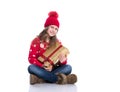 Charming smiling little girl with curly hairstyle wearing red knitted sweater and hat holding christmas gift isolated on white. Royalty Free Stock Photo