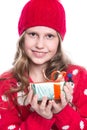 Charming smiling little girl with curly hairstyle wearing red knitted sweater and hat holding christmas gift isolated on white. Royalty Free Stock Photo