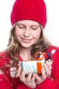 Charming smiling little girl with curly hairstyle wearing red knitted sweater and hat holding christmas gift isolated on white. Royalty Free Stock Photo