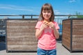 A charming smiling little girle is holding a hamburger in the open air on a sunny day